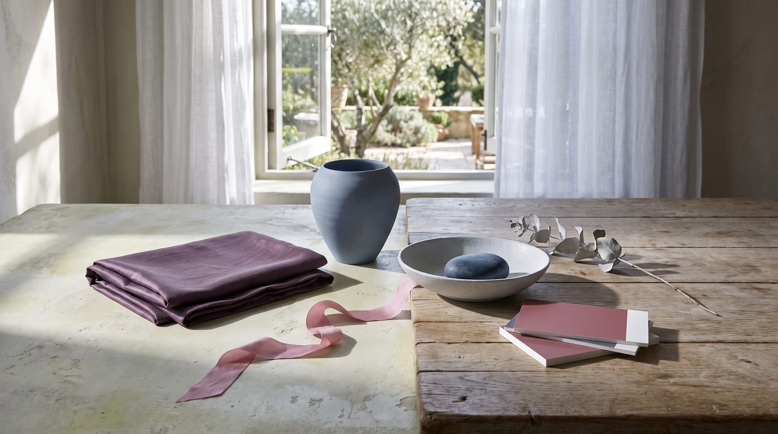 A cool summer editorial still-life: folded slate-blue linen, a small matte ceramic vessel in cool gray, a sprig of dusty lavender, and a smooth river stone on cool pale plaster, every element rendered in the palette's slate blues, cool roses, mauves, and soft summer whites.