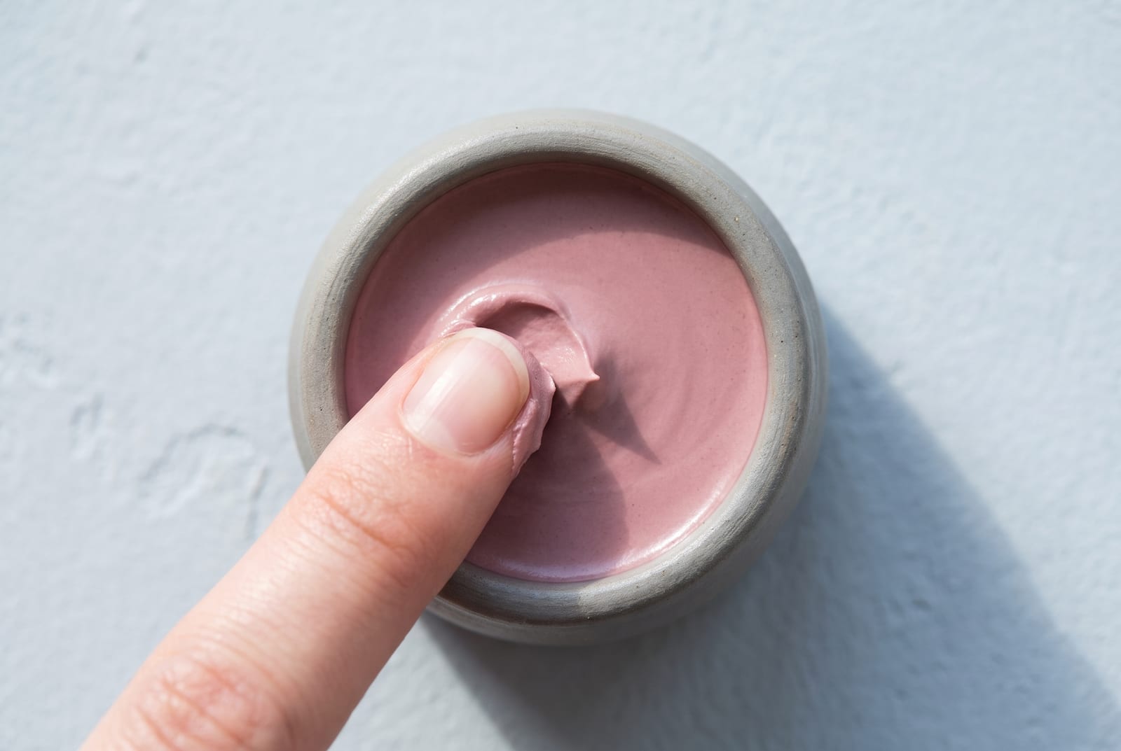 A cool summer beauty macro: a single palette-hex pigment detail at extreme close-up, a cool rose or soft mauve cream, caught in soft flat daylight against a cool plaster background.