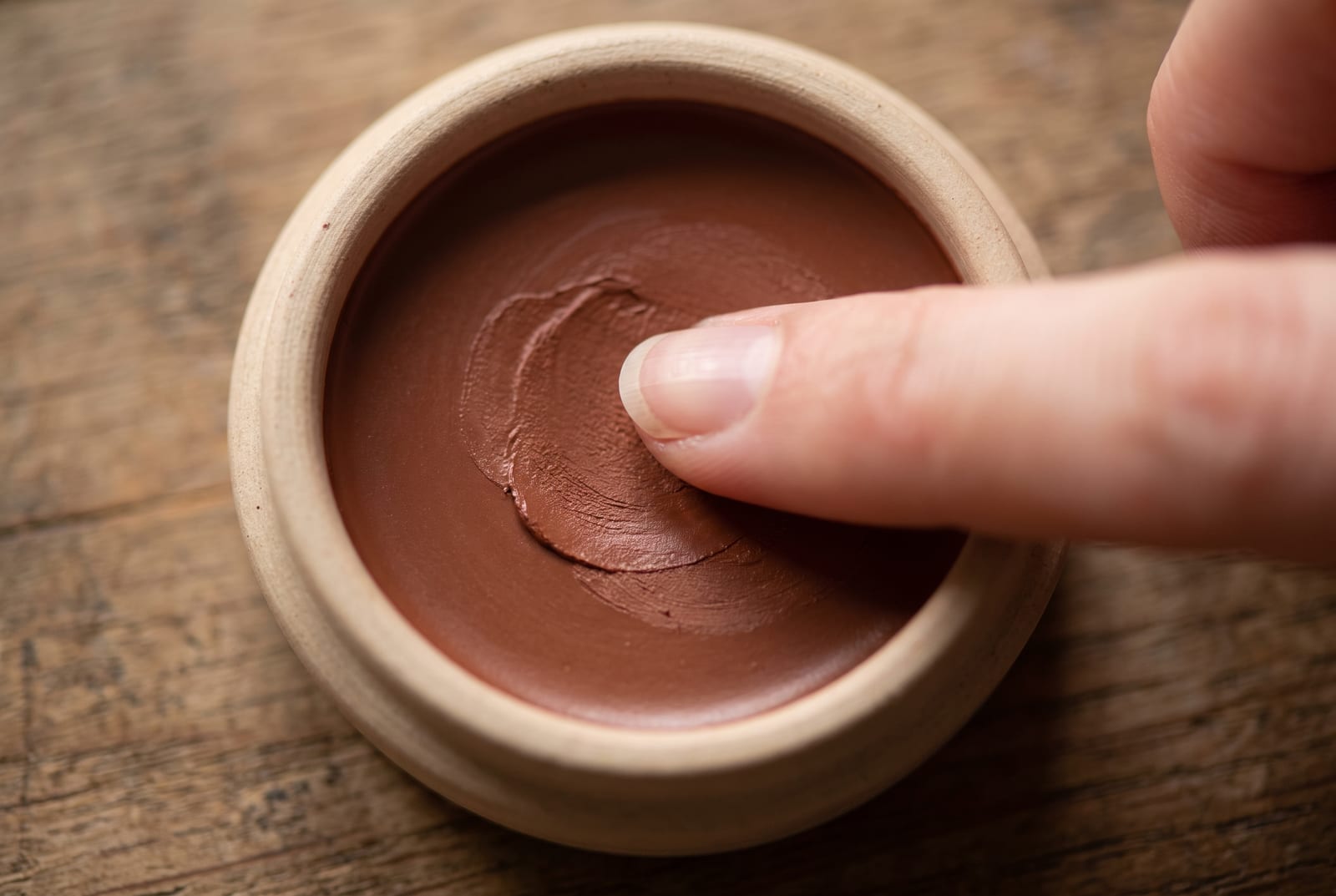 A warm autumn beauty macro: a single palette-hex pigment detail at extreme close-up, a copper-rust eyeshadow or a terracotta lip, caught in soft directional daylight against a matte plaster background.