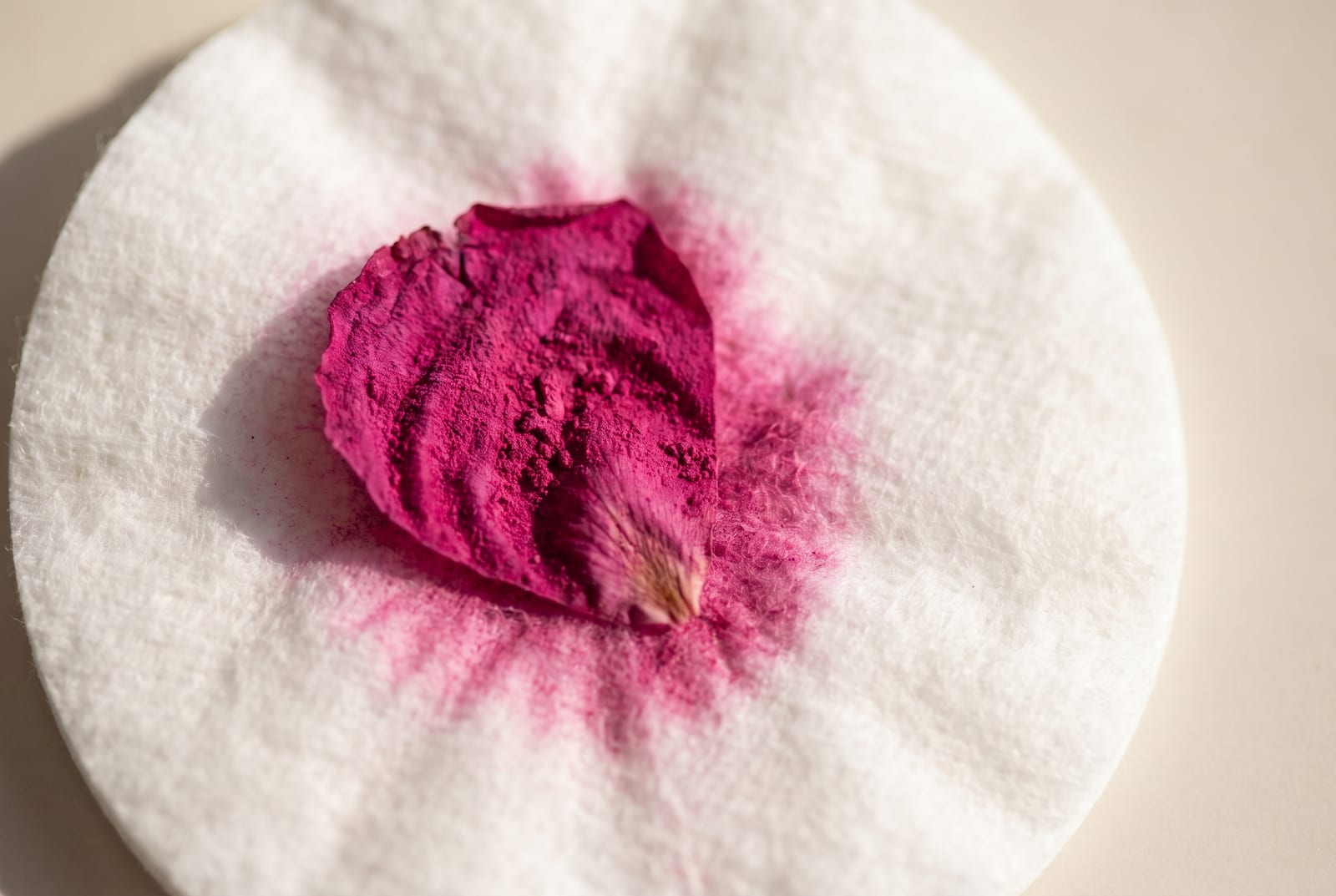 A bright winter beauty macro: a single palette-hex pigment detail at extreme close-up, a blue-red lip cream against a matte black background, caught in hard cool directional light.