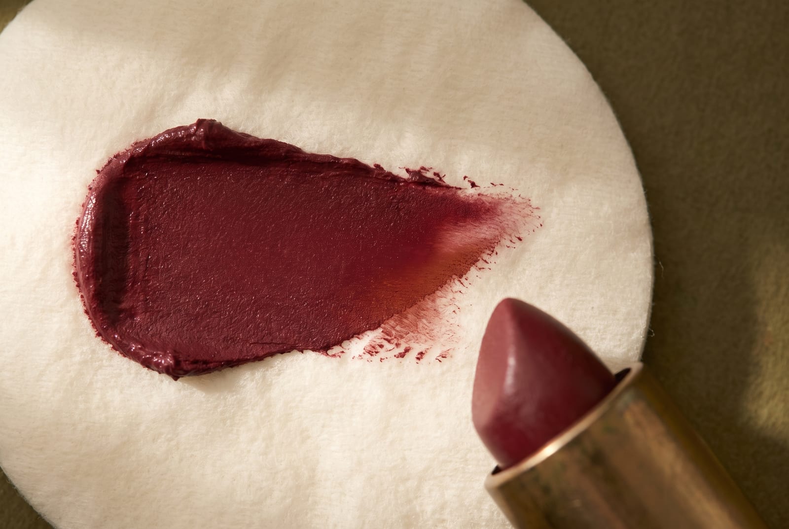 A deep autumn beauty macro: a single palette-hex pigment detail at extreme close-up, a smear of burnished bronze or deep brick, caught in low directional daylight against a dark matte background.
