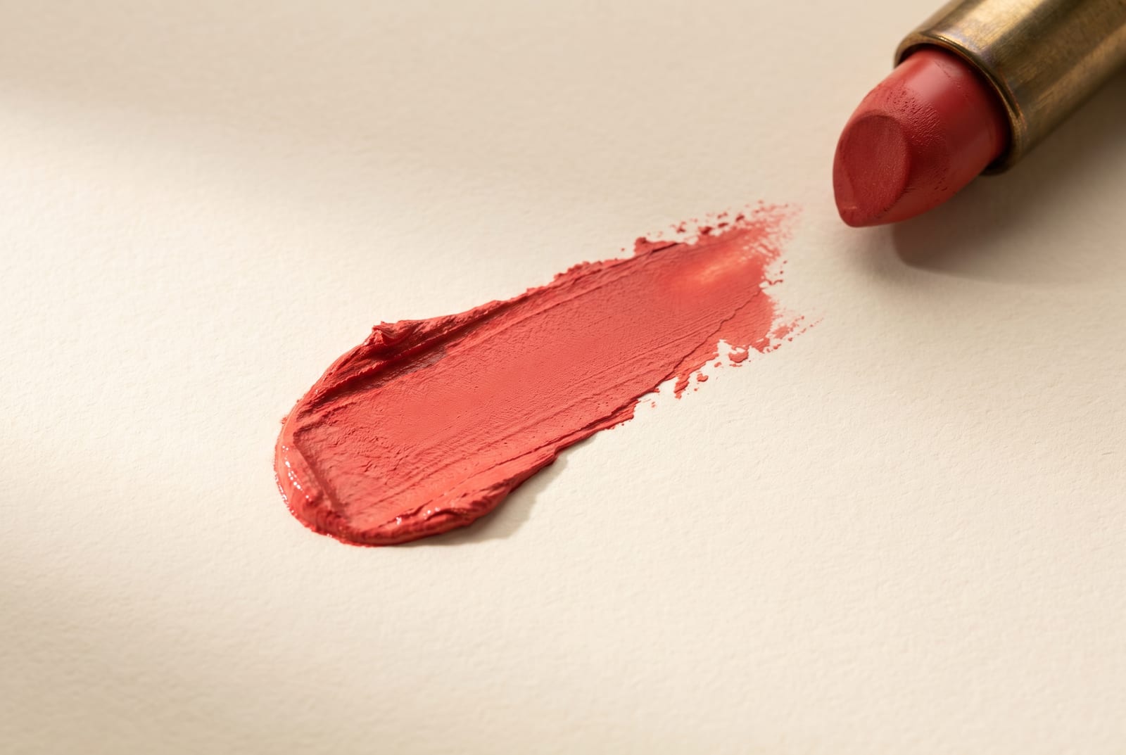 A warm spring beauty macro: a single palette-hex pigment detail at extreme close-up, a coral blush or a golden-peach eyeshadow, caught in soft directional daylight against a warm cream plaster background.