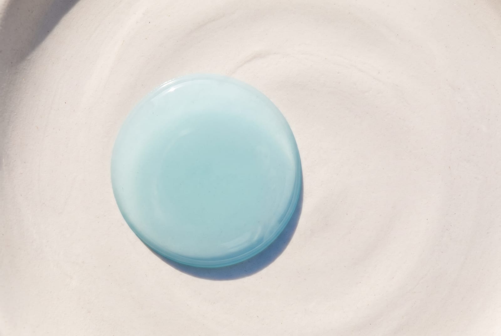A light summer beauty macro: a single palette-hex pigment detail at extreme close-up, caught in soft, flat daylight against a cool plaster background.