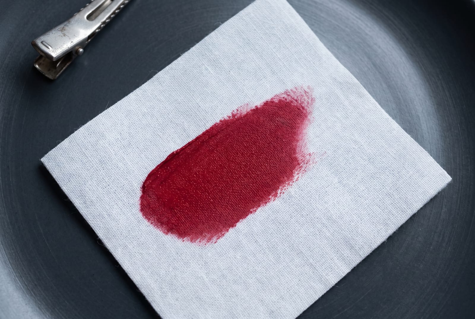 A cool winter beauty macro: a single palette-hex pigment detail at extreme close-up, a cool cherry red or fuchsia cream, caught in hard directional light against a pure-white background.