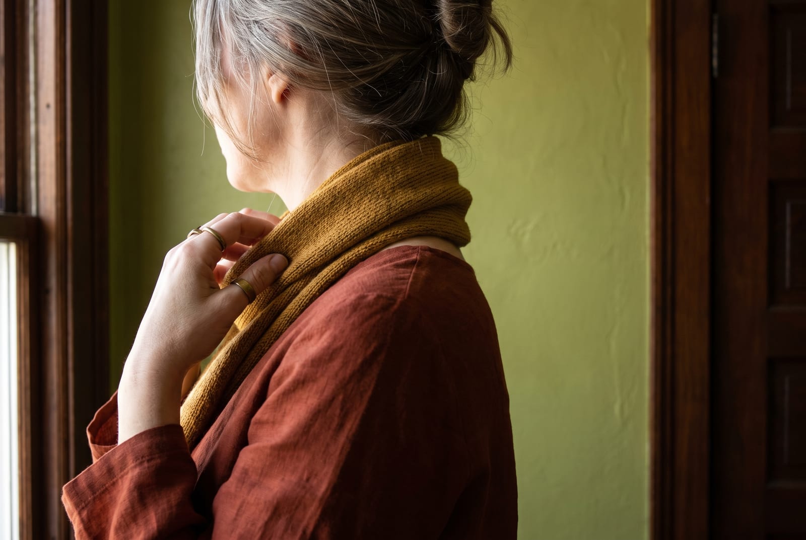 A warm autumn portrait detail: a face-free editorial crop showing rich auburn hair against a rust garment in golden side-lit daylight, the kind of private, considered frame fashion editorials use when the face is out of view.