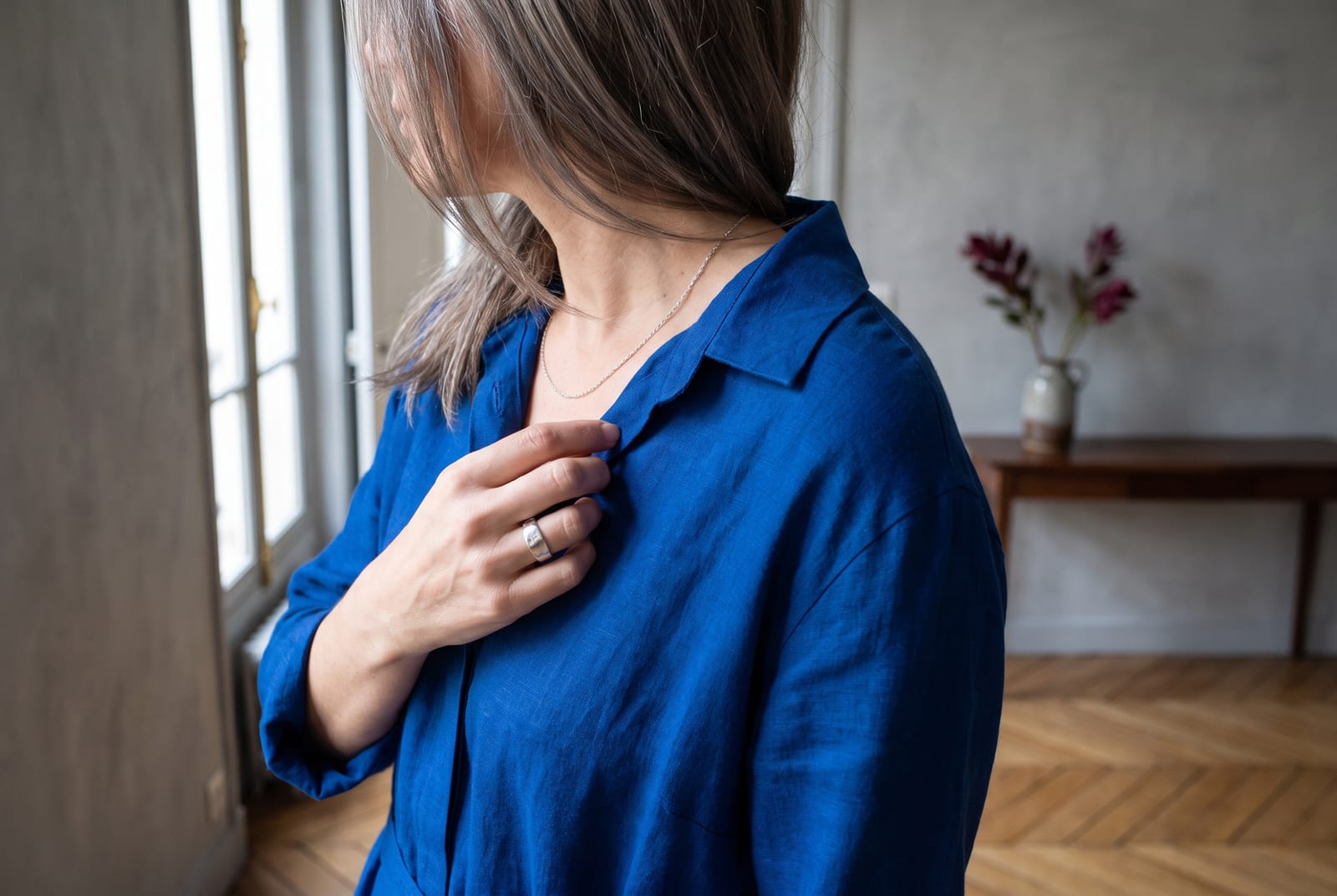 A bright winter portrait detail: a face-free editorial crop showing blue-black hair against a stark white collar in hard cool daylight, a sliver of electric-cobalt visible at the shoulder, the kind of high-contrast frame fashion editorials use when the face is out of view.
