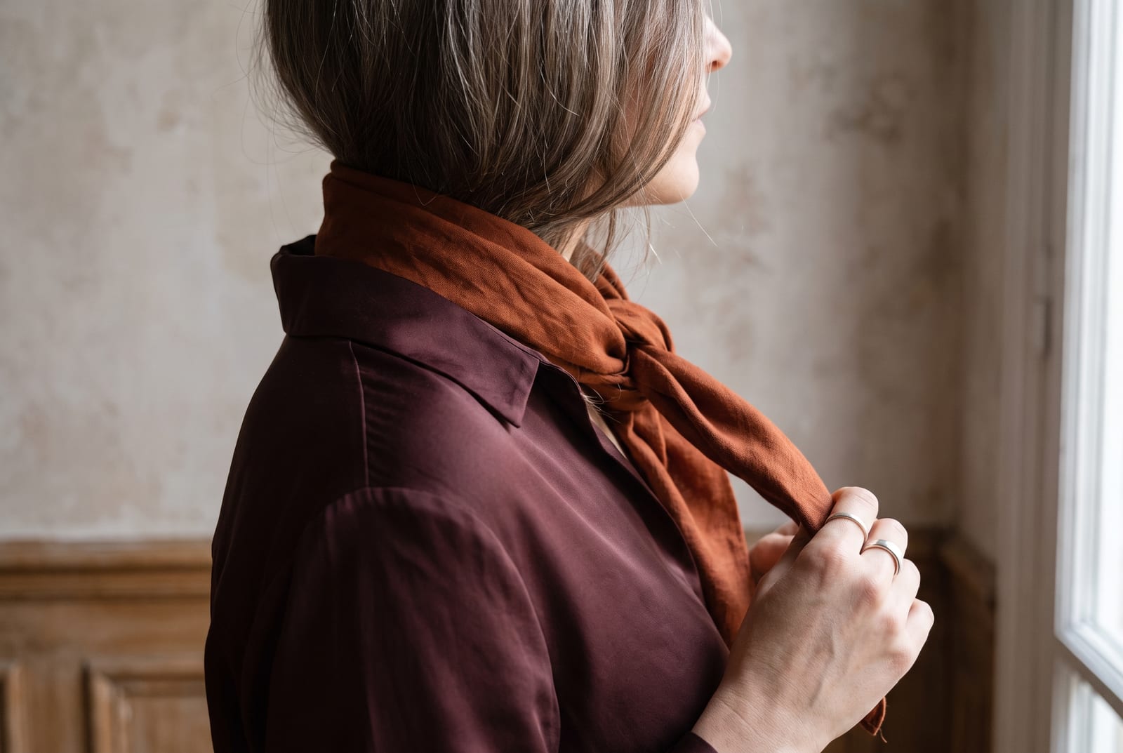 A deep autumn portrait detail: a face-free editorial crop showing dark warm hair against a chocolate-brown garment in low, warm side-lit daylight, the kind of private, considered frame fashion editorials use when the face is out of view.