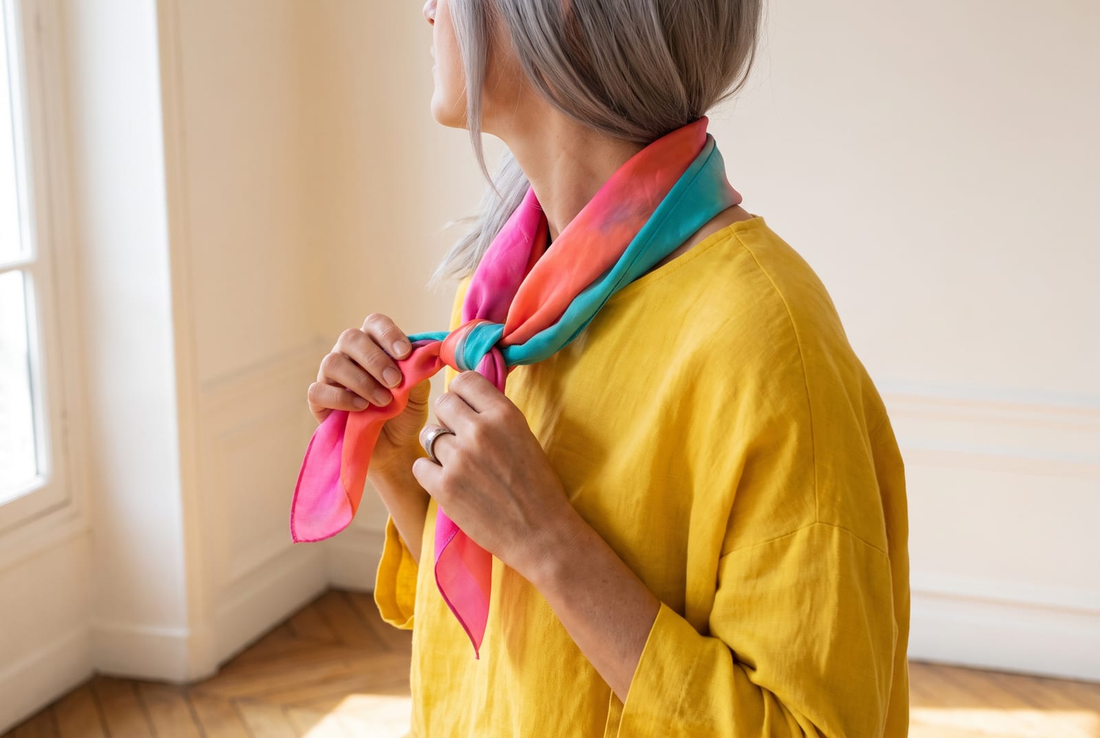 A bright spring portrait detail: a face-free editorial crop showing warm golden-red hair against a clear coral garment in bright, even side-lit daylight, the kind of private, considered frame fashion editorials use when the face is out of view.