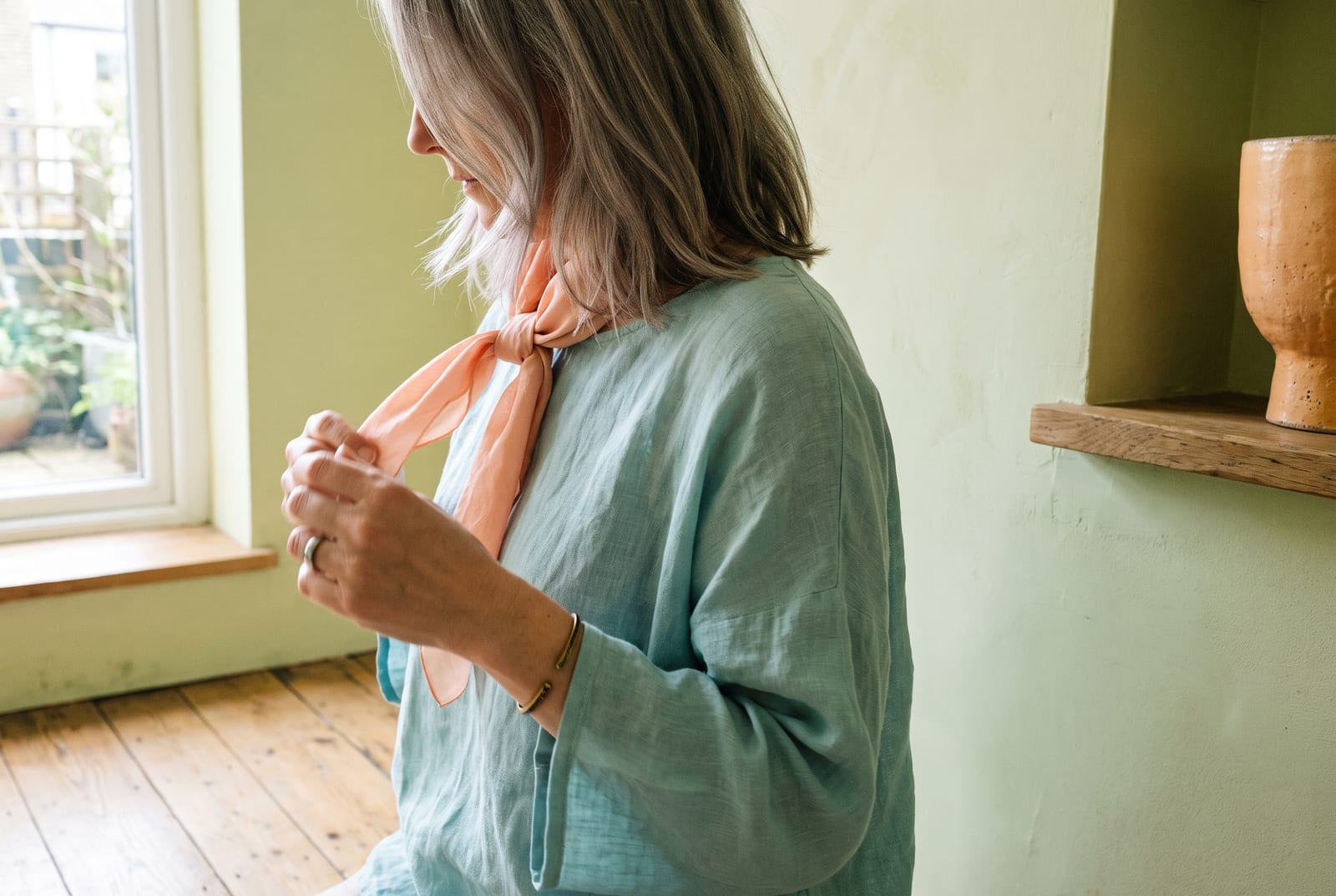 A light spring portrait detail: a face-free editorial crop showing light golden hair against a peach garment in soft, bright morning daylight, the kind of clean, luminous frame fashion editorials use when the face is out of view.