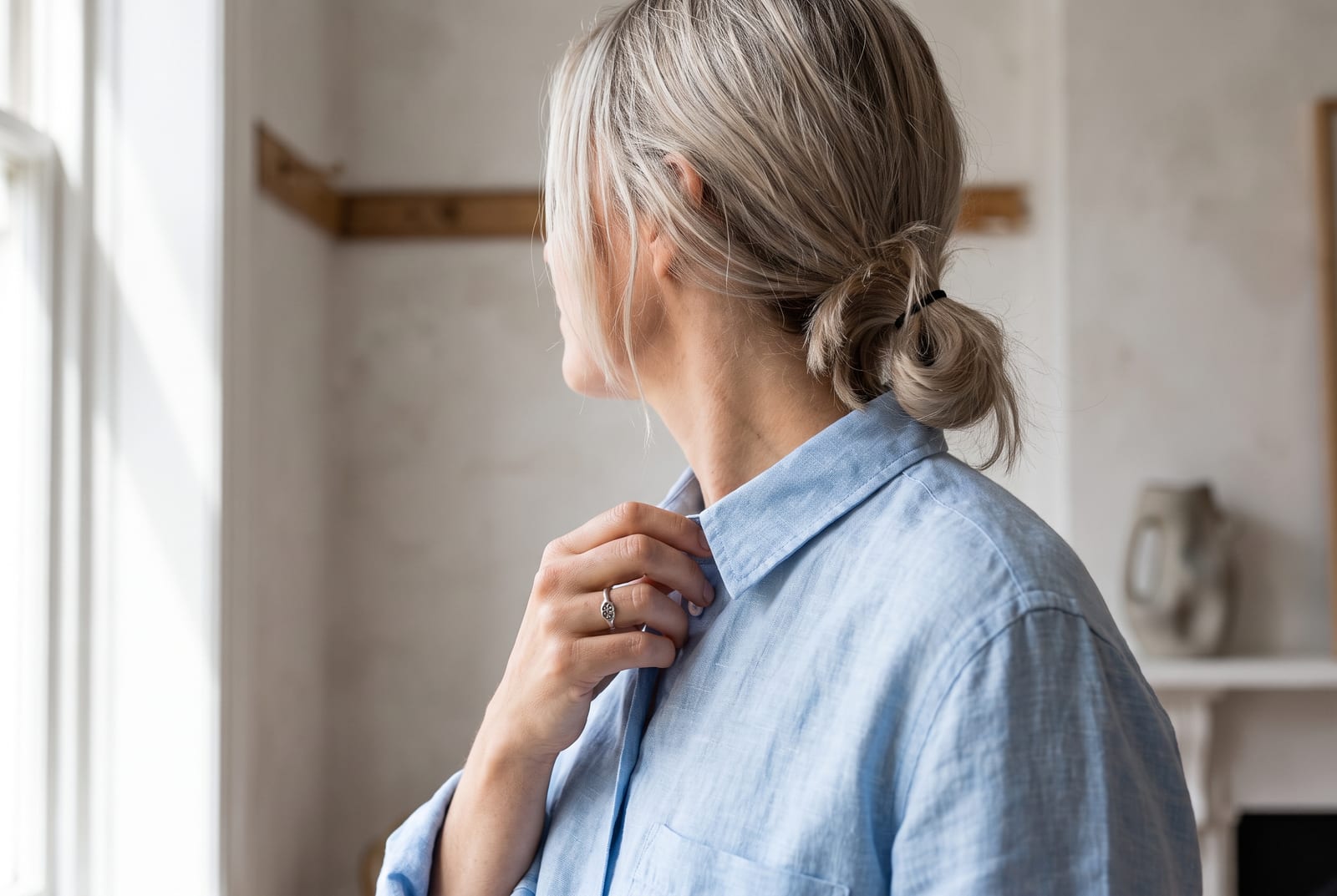 A light summer portrait detail: a face-free editorial crop showing cool ash-blonde hair against a powder-blue garment in soft, flat, north-facing daylight, the kind of quiet frame fashion editorials use when the face is out of view.