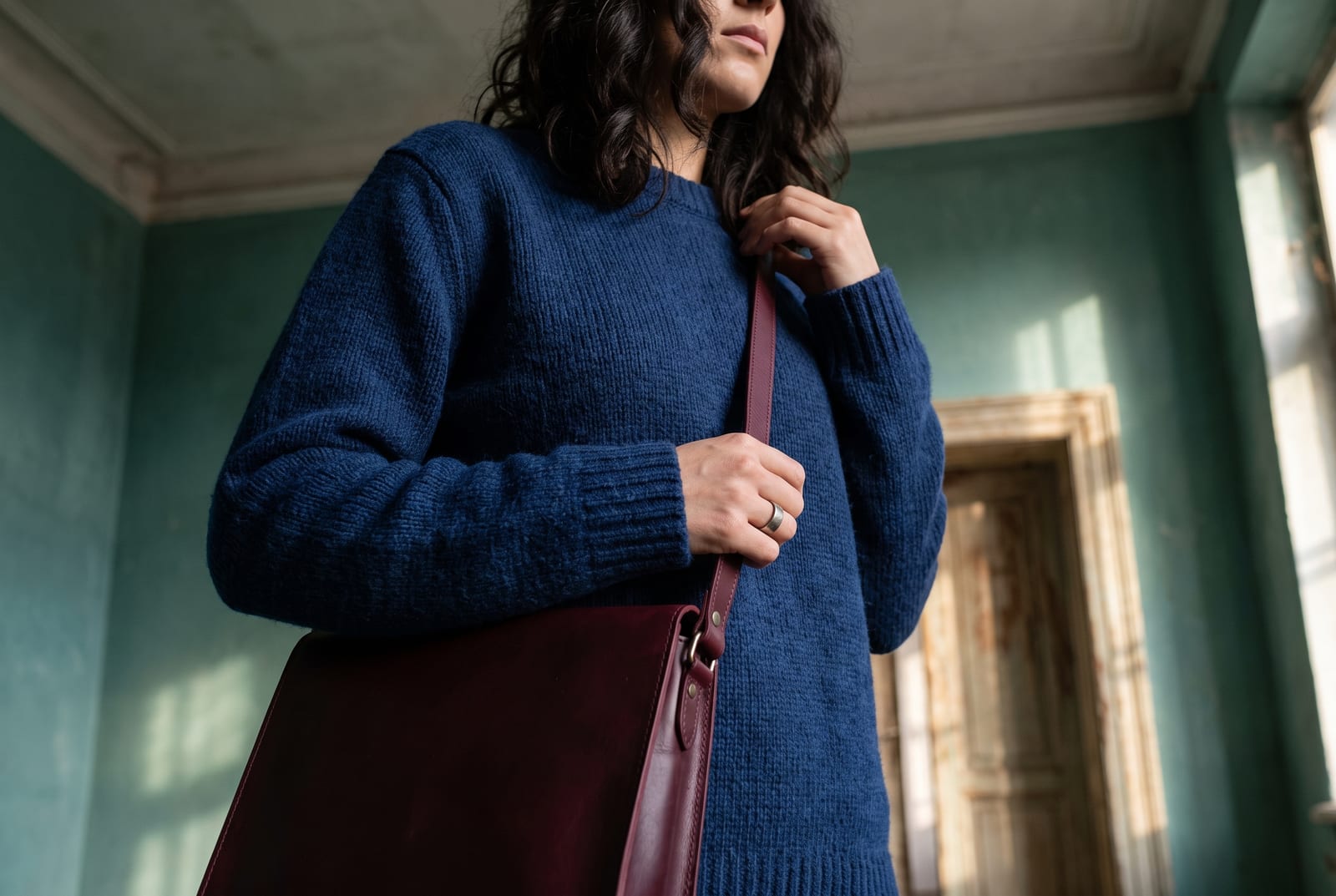 A deep winter worn detail: a cropped-figure composition showing a palette-hex emerald, sapphire, or blue-red piece worn close to the body against black, in hard cool side-lit daylight, face out of frame in the style of catalog editorial.