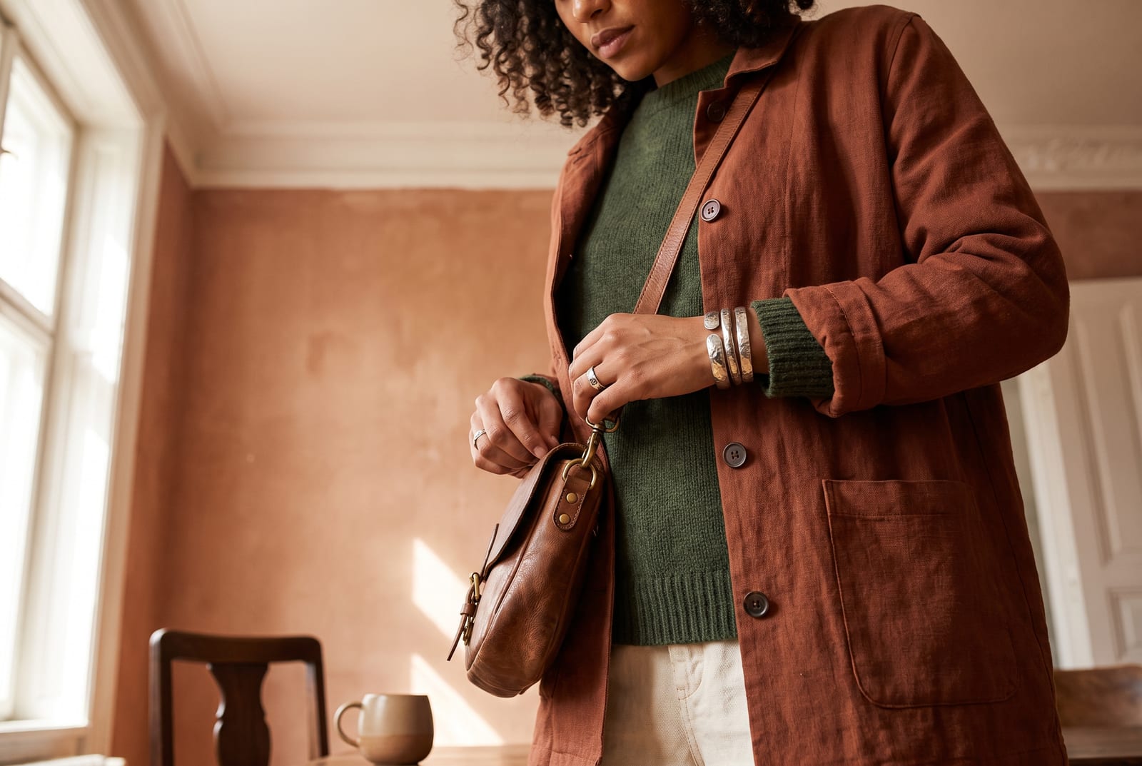 A warm autumn worn detail: a cropped-figure composition showing a palette-hex rust, olive, or golden-brown piece worn close to the body in golden side-lit daylight, face out of frame in the style of catalog editorial.